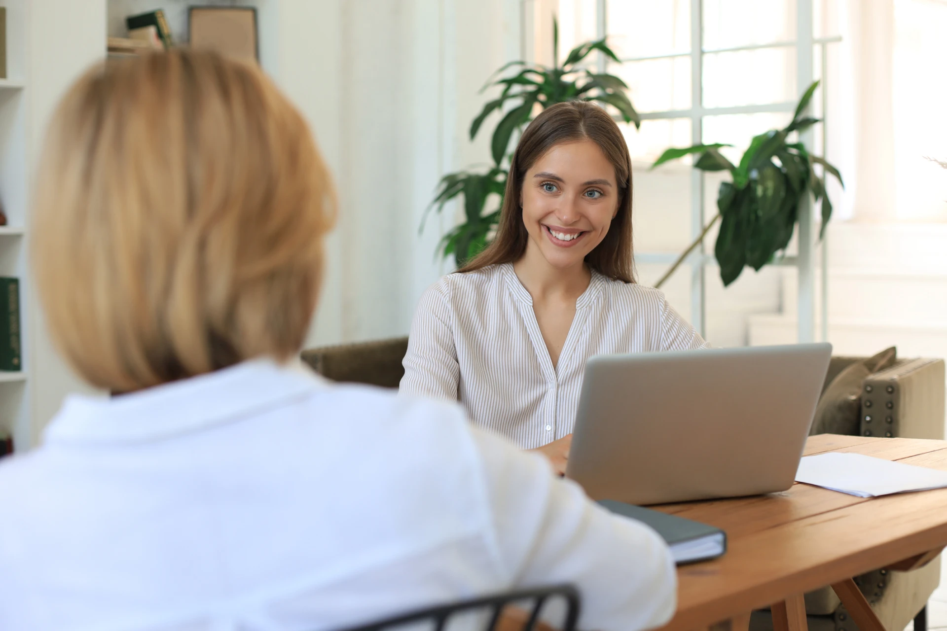 Woman smiling during a face-to-face consultation while working on a laptop in a bright office.